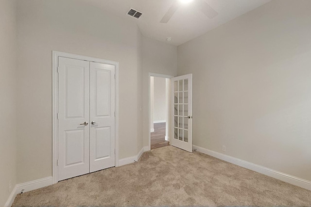 unfurnished bedroom featuring light carpet, baseboards, a closet, french doors, and a ceiling fan