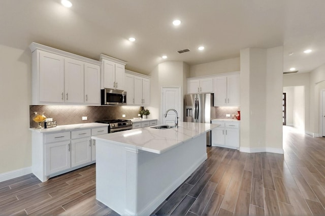 kitchen featuring a sink, stainless steel appliances, wood finished floors, decorative backsplash, and an island with sink