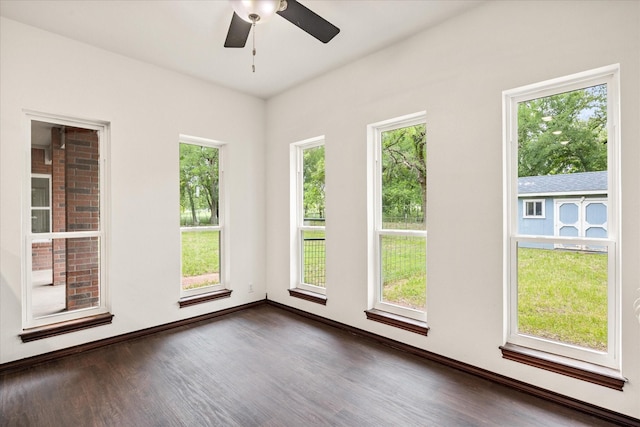unfurnished room featuring dark wood-type flooring, a ceiling fan, healthy amount of natural light, and baseboards