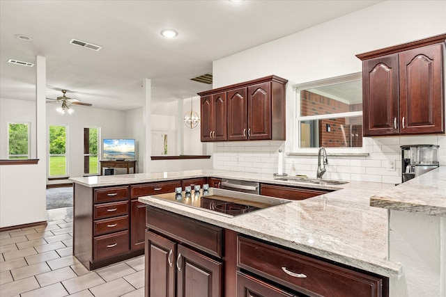 kitchen with a sink, a peninsula, light stone countertops, and backsplash