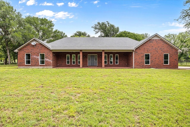 rear view of property with brick siding, a lawn, and roof with shingles