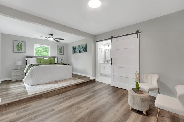 bedroom with a barn door, wood finished floors, baseboards, connected bathroom, and a ceiling fan