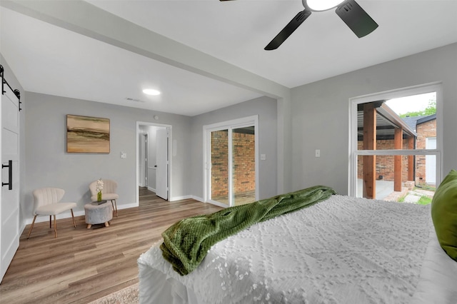 bedroom with a barn door, light wood-style flooring, baseboards, and a ceiling fan