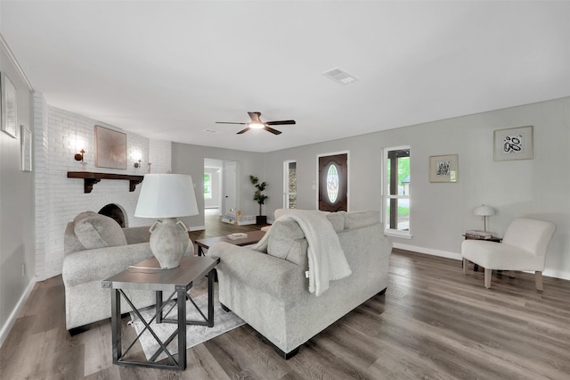 living area with baseboards, dark wood-style flooring, a ceiling fan, and a brick fireplace