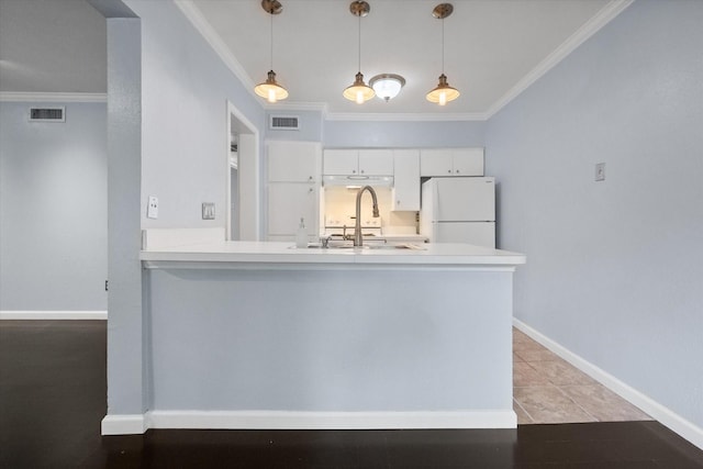 kitchen with freestanding refrigerator, a sink, crown molding, white cabinetry, and a peninsula