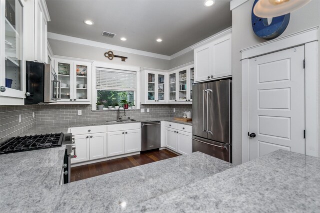 kitchen featuring appliances with stainless steel finishes, a sink, decorative backsplash, white cabinetry, and light stone counters