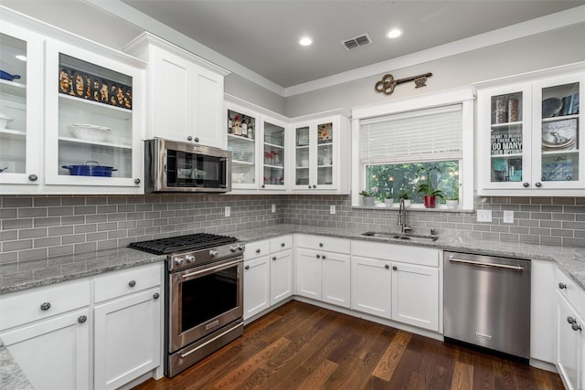 kitchen with appliances with stainless steel finishes, a sink, white cabinetry, decorative backsplash, and dark wood-type flooring