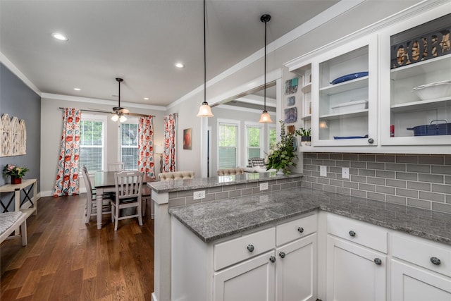 kitchen with a peninsula, crown molding, white cabinetry, dark wood-type flooring, and tasteful backsplash
