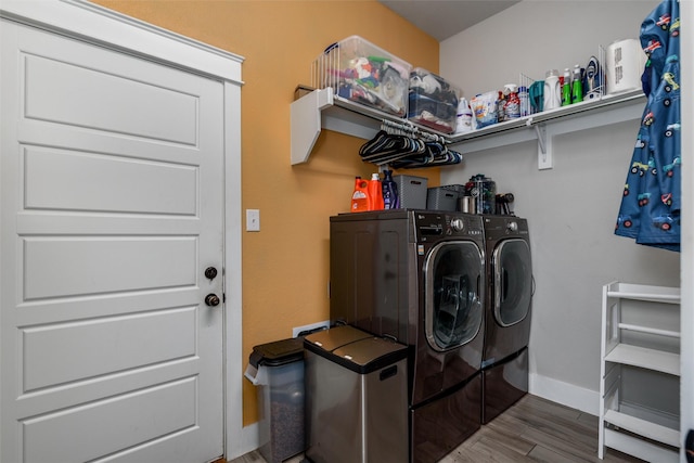 clothes washing area featuring washing machine and dryer, wood finished floors, and baseboards