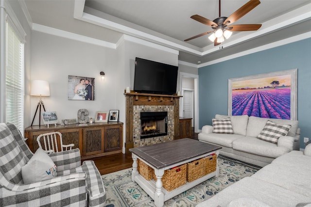 living area with a tray ceiling, a ceiling fan, wood finished floors, and a warm lit fireplace