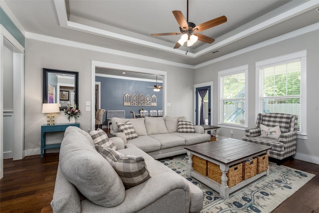 living area with a raised ceiling, a ceiling fan, dark wood-style flooring, and baseboards