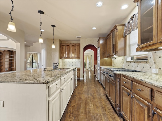 1413 Prairie Dr, Carrollton, TX 75007 - kitchen featuring arched walkways, a sink, stainless steel appliances, glass insert cabinets, and light stone counters