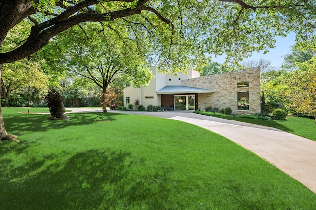 view of front facade featuring a front lawn, stone siding, metal roof, and a standing seam roof
