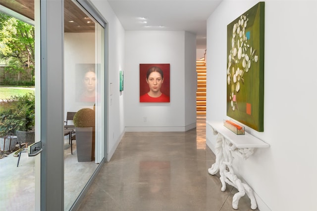 hallway with concrete floors, stairway, and baseboards