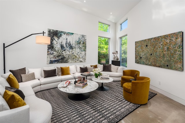 living room featuring finished concrete flooring, a towering ceiling, and baseboards