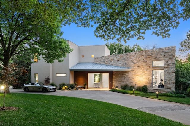 contemporary house with a front yard, stone siding, driveway, a standing seam roof, and metal roof