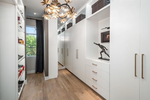 walk in closet with light wood finished floors and a chandelier