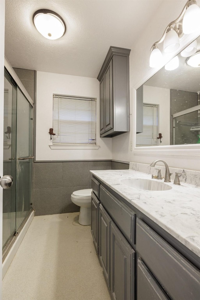 204 E 2nd St, Quinlan, TX 75474 - full bathroom with tile walls, a stall shower, vanity, toilet, and wainscoting