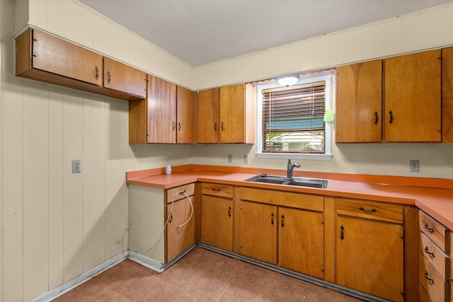 kitchen with a sink, brown cabinets, light countertops, and light tile patterned floors