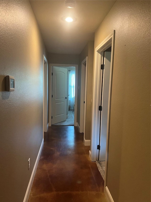 hallway with baseboards, concrete floors, and a textured wall