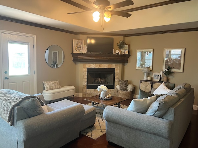 living room featuring ceiling fan, crown molding, baseboards, a tile fireplace, and dark wood-style floors
