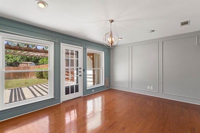 unfurnished dining area featuring a decorative wall, a chandelier, and wood finished floors
