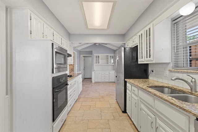 kitchen with stainless steel appliances, a sink, white cabinets, and stone tile flooring
