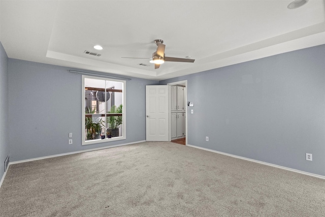 empty room with a raised ceiling, carpet, baseboards, and a ceiling fan