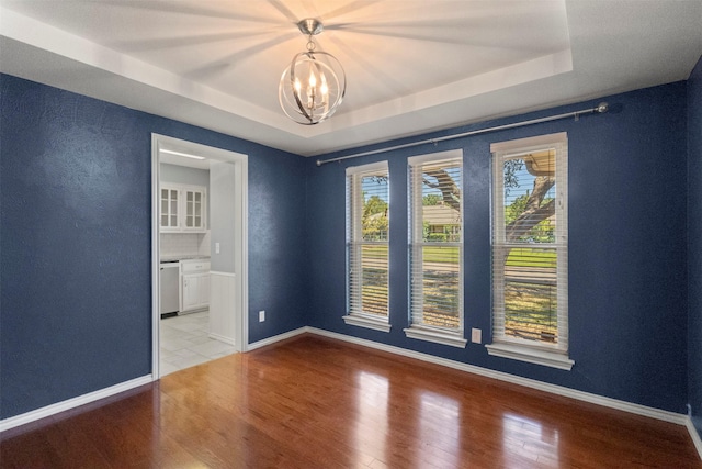 empty room featuring a raised ceiling, a chandelier, light wood-style floors, baseboards, and a textured wall