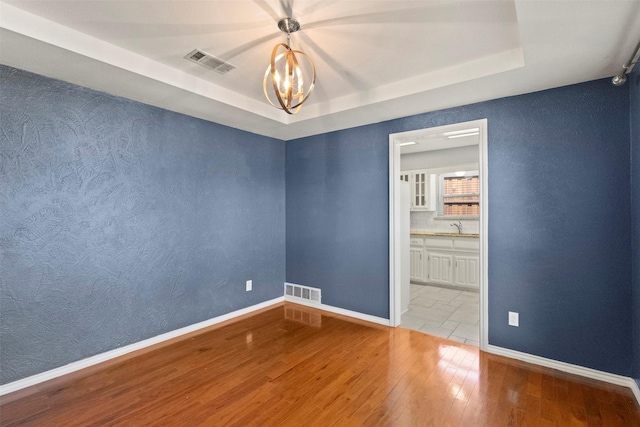 empty room featuring a tray ceiling, a chandelier, hardwood / wood-style flooring, baseboards, and a sink