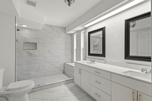 bathroom with marble look tile flooring, toilet, tiled shower, and double vanity