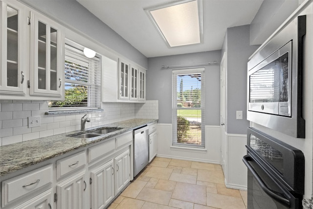 kitchen with a sink, appliances with stainless steel finishes, white cabinetry, a wainscoted wall, and light stone countertops