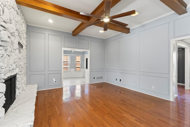 unfurnished living room featuring a decorative wall, a ceiling fan, beam ceiling, wood finished floors, and a fireplace