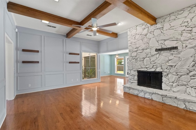 unfurnished living room featuring a decorative wall, a ceiling fan, wood finished floors, beamed ceiling, and a stone fireplace