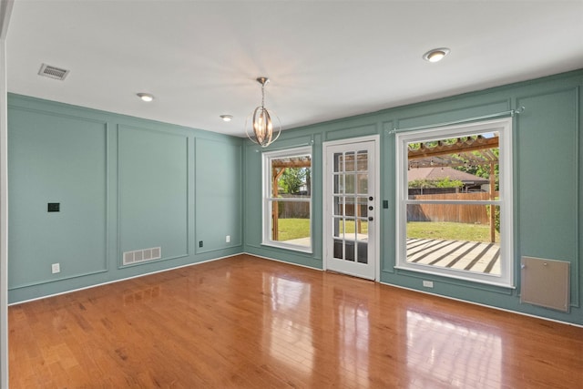 unfurnished dining area featuring a decorative wall, plenty of natural light, wood finished floors, and a chandelier