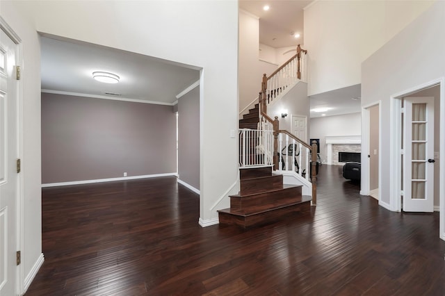 foyer entrance featuring stairs, wood finished floors, a fireplace, baseboards, and crown molding