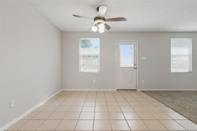 unfurnished room with a textured ceiling, a ceiling fan, light tile patterned floors, and baseboards