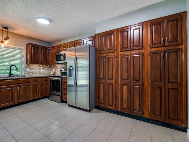 kitchen featuring appliances with stainless steel finishes, a sink, a textured ceiling, backsplash, and stone countertops