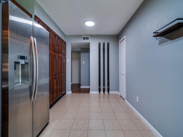 kitchen featuring stainless steel refrigerator with ice dispenser, a textured ceiling, light tile patterned flooring, and baseboards