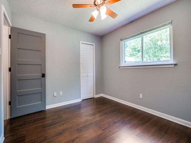 unfurnished bedroom featuring baseboards, dark wood-style flooring, a closet, a textured ceiling, and a ceiling fan