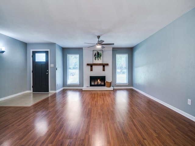unfurnished living room with ceiling fan, baseboards, a fireplace, and wood finished floors