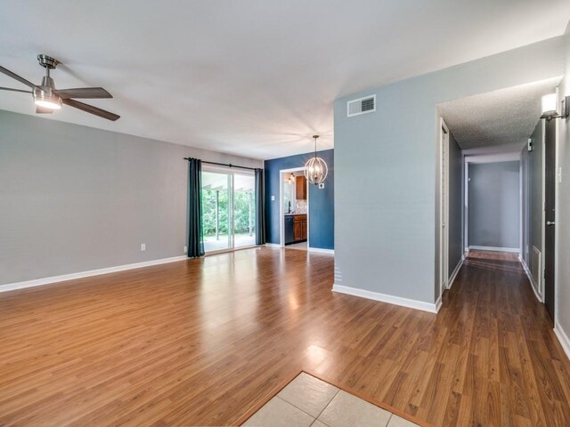 unfurnished room with a chandelier, a ceiling fan, wood finished floors, and baseboards