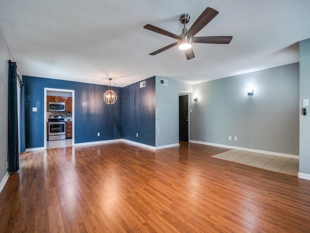 unfurnished living room with a chandelier, a ceiling fan, wood finished floors, and baseboards