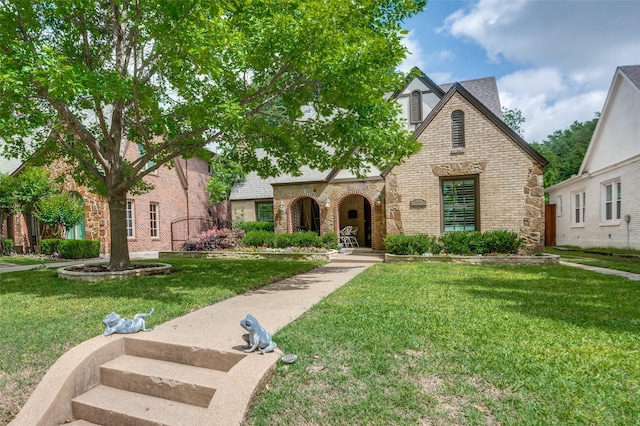 tudor house featuring a front lawn, stone siding, and brick siding