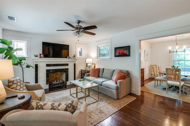 living room with hardwood / wood-style floors, ceiling fan, a stone fireplace, baseboards, and a chandelier