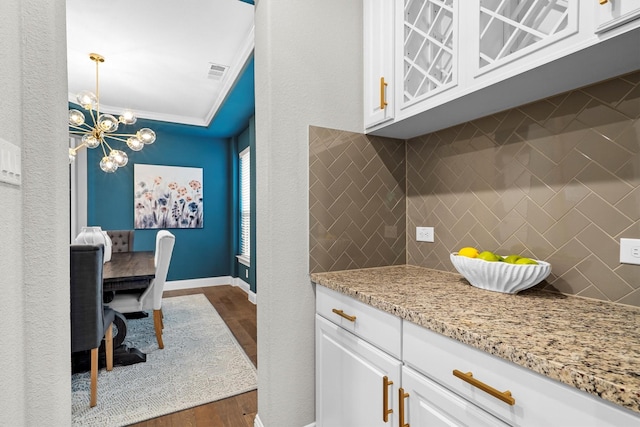 kitchen featuring dark wood-style floors, white cabinets, a chandelier, backsplash, and ornamental molding