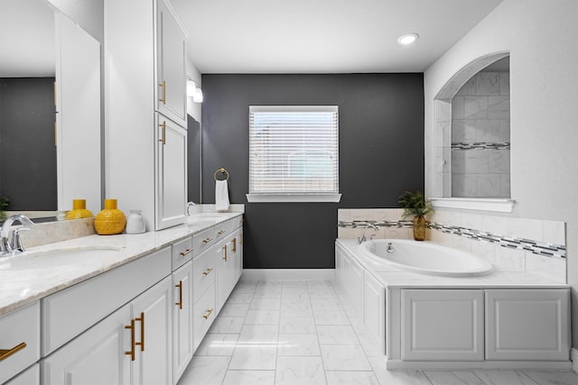 full bath with marble look tiles, a garden tub, double vanity, baseboards, and recessed lighting