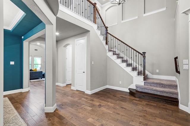 entryway with arched walkways, wood finished floors, stairway, baseboards, and a high ceiling