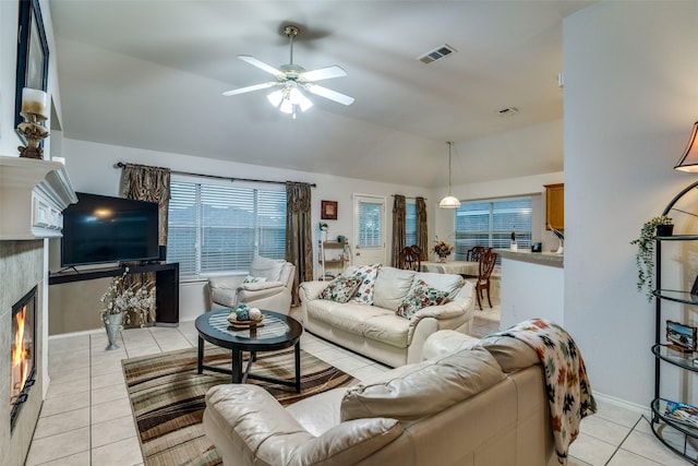living room with light tile patterned floors, lofted ceiling, a warm lit fireplace, ceiling fan, and baseboards