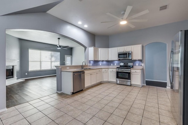 kitchen featuring appliances with stainless steel finishes, a ceiling fan, arched walkways, a sink, and open floor plan